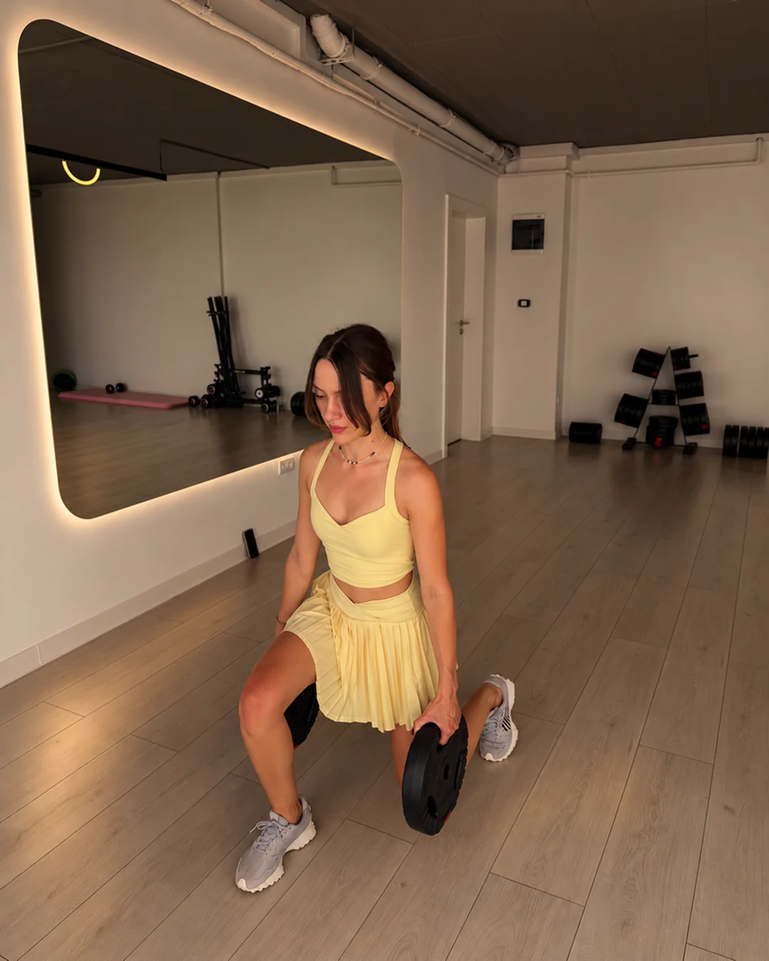 Exercițiu de fandare cu un disc de greutăți, în ținută galbenă, la XPilates